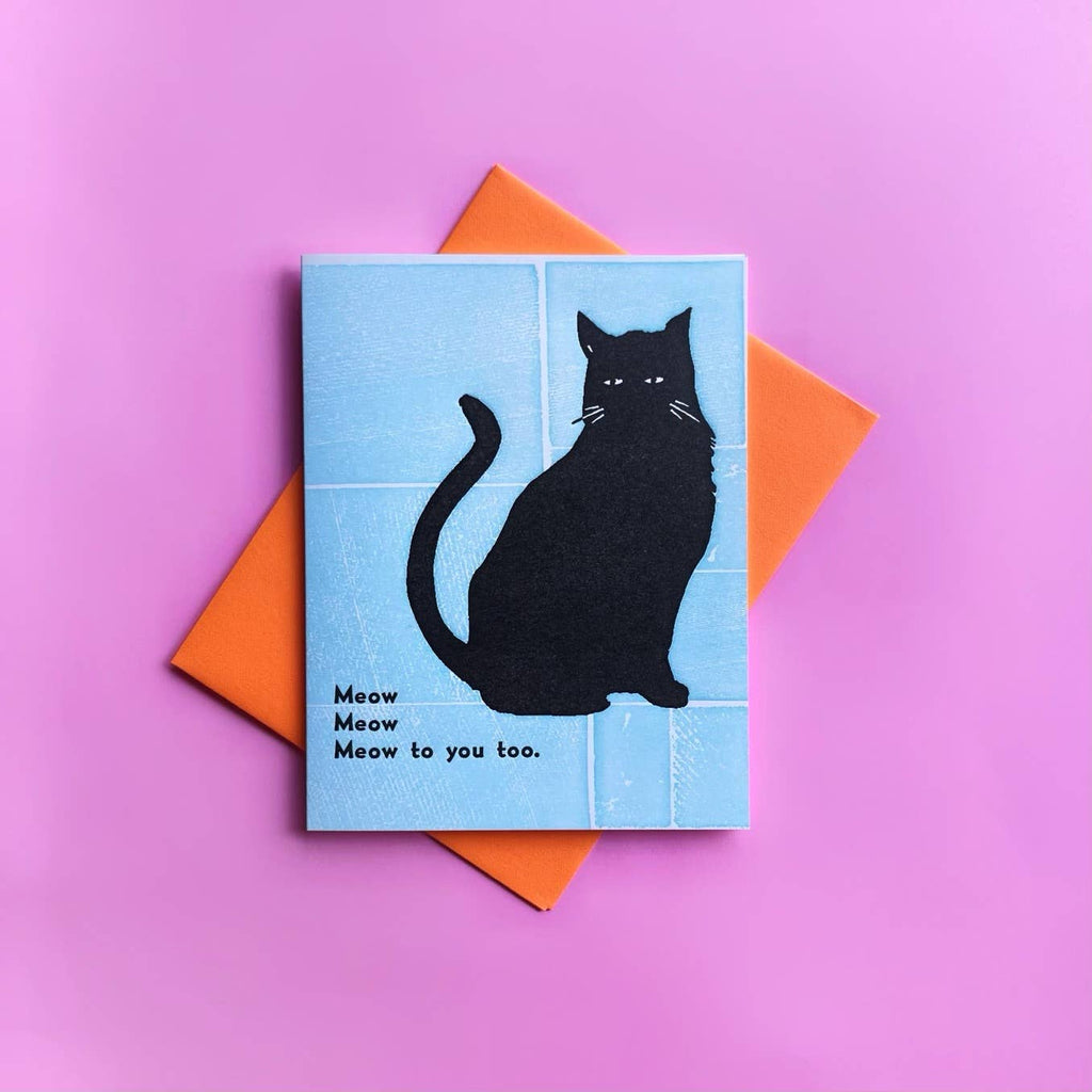 Light blue background with image of a black cat with black text says, “Meow Meow Meow to you too”. Orange envelope included.    