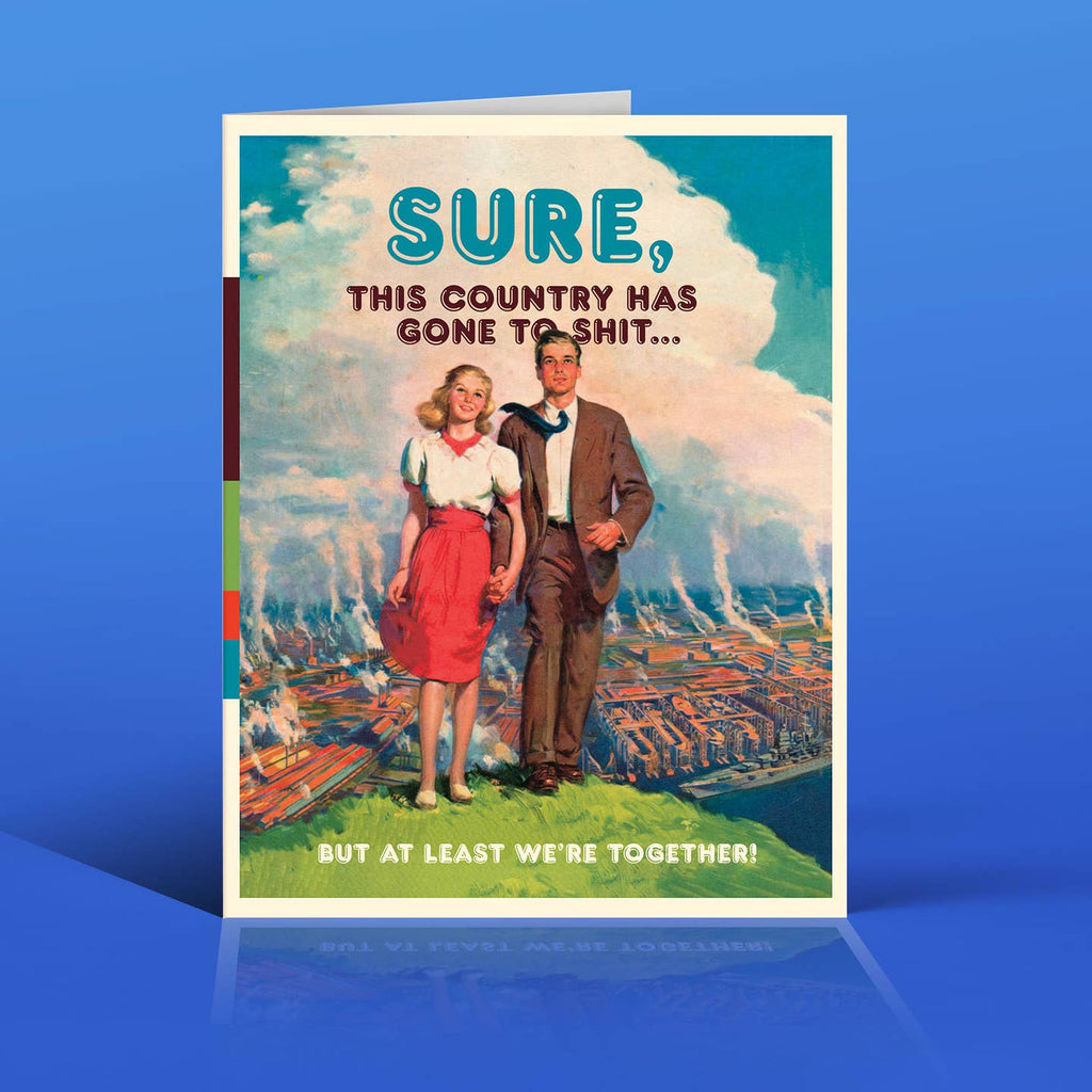 Greeting card with blue and white background and image of a man and a woman holding hands. Blue and brown text says, "Sure, this country has gone to shit...but at least we're together!". Envelope included.