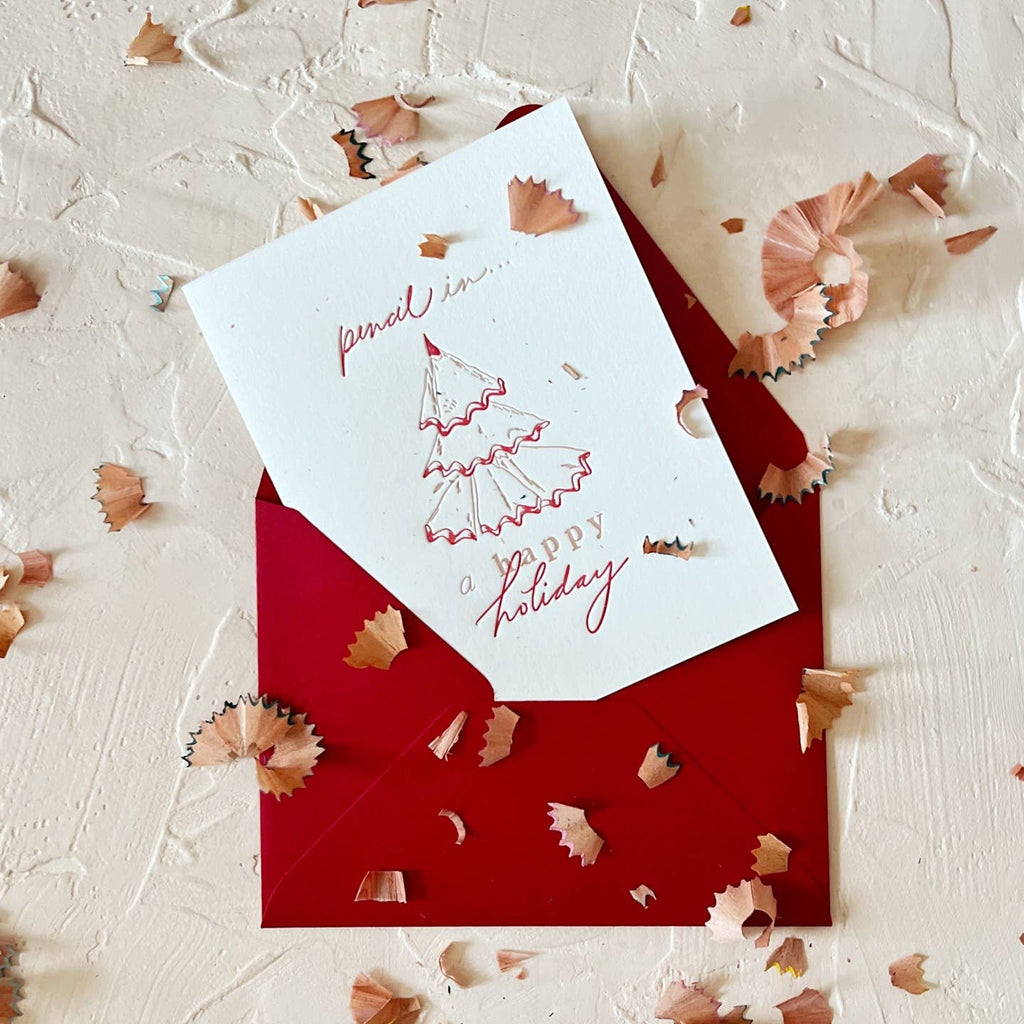 Greeting card with white background and image of a tree made from pencil shavings with red text says, "Pencil in...a happy holiday". Red envelope included.