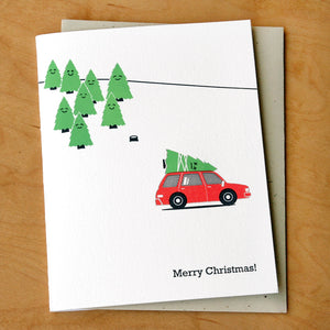 Greeting card with white background with images of green trees and red car with dead green tree on top of it. Black text says, "Merry Christmas!". Envelope included.