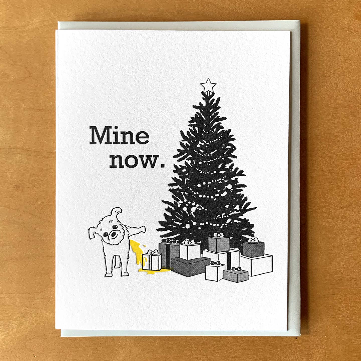 Greeting card with white background and image of a Christmas tree with presents underneath and image of a dog lifting its leg and peeing on the presents. Black text says, "Mind now.". Envelope included. 