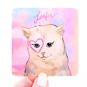 Image of a sticker with a pink and blue background and a tan cat with a pink heart drawn around the right eye and pink text says, "Loafer". 