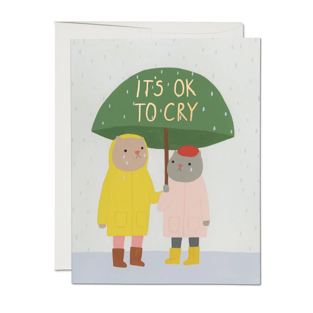 White background with images of two cats holding a green umbrella wearing raincoats and crying. Yellow text say, "It's OK to cry". White envelope included.