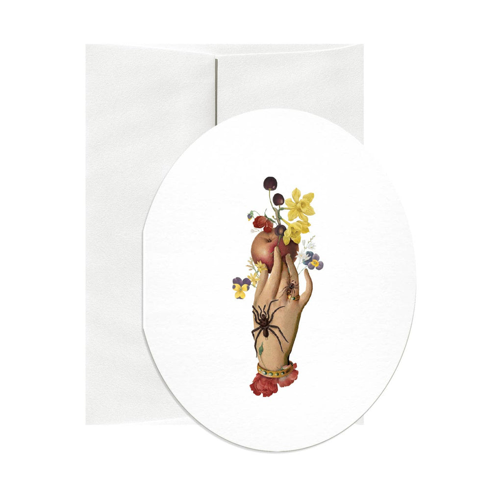 Oval greeting card with white background and image of a hand holding an apple and flowers with a black spider crawling on the hand. Envelope included. 
