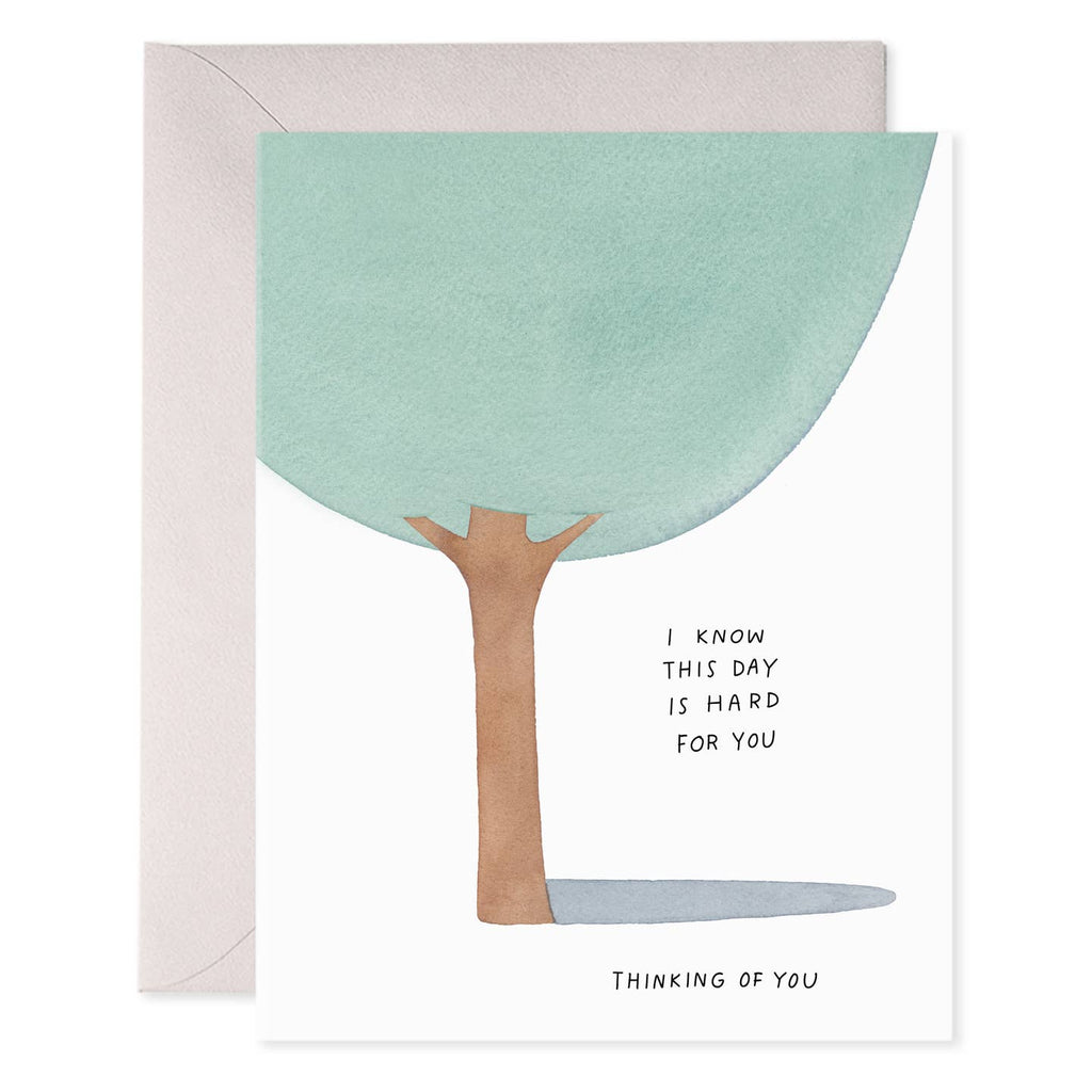 Greeting card with white background and image of a tree with black text says, "I know this day is hard for you, thinking of you". Grey envelope included. 