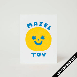 White background with image of yellow smiley face with blue stars for eyes and mouth. Blue text says, "Mazel Tov". Kratt envelope included.