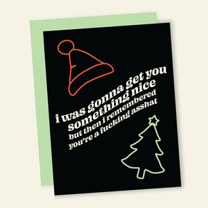 Black background with red outline of Santa hat and green outline of holiday tree. White text says, "I was gonna get you something nice but then remember you're a fucking asshat". Green envelope is included. 