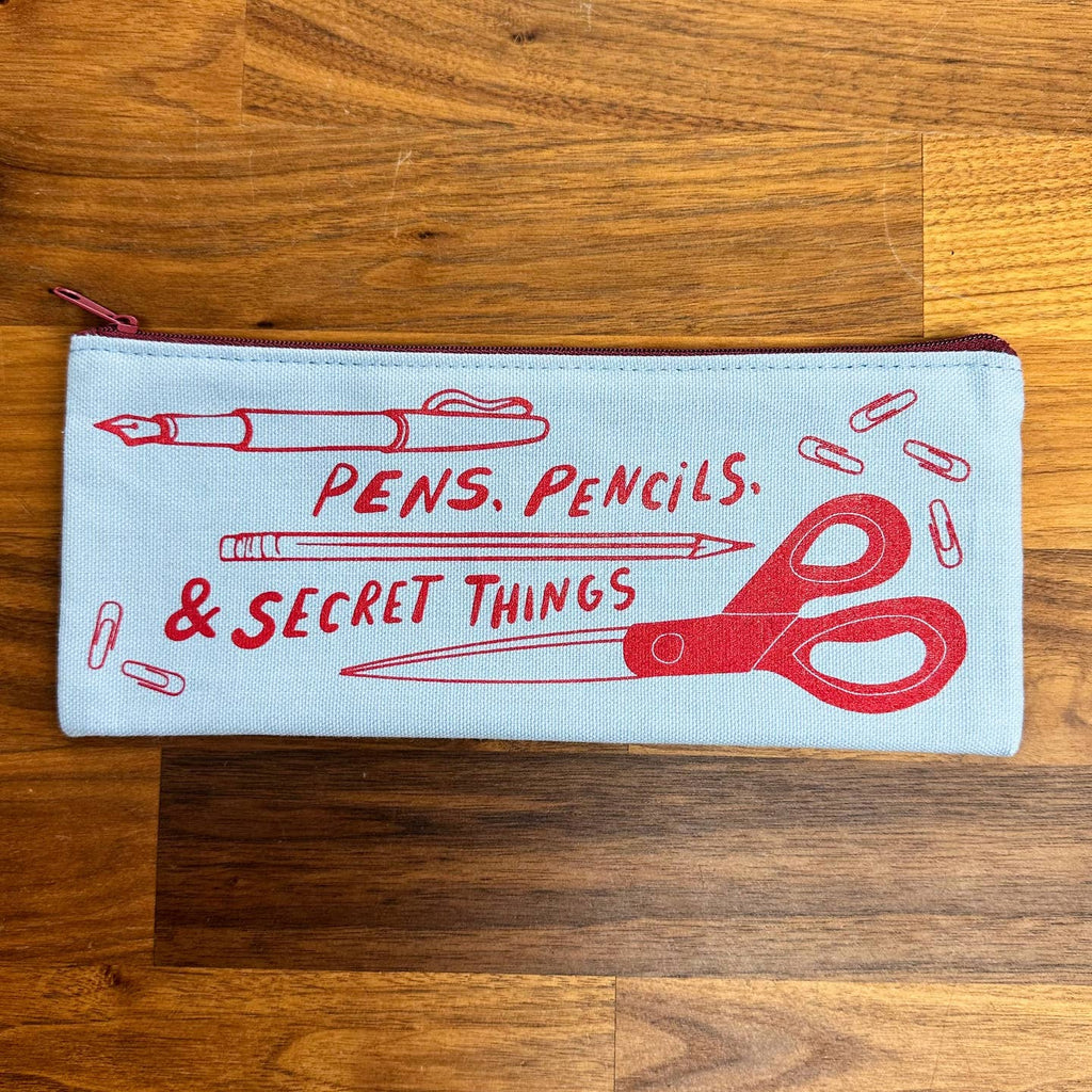Image of canvas zippered pencil case with cream background and images of fountain pen, pencil, scissors and paper clips in red. Red text says, "Pens, pencils & secret things". 