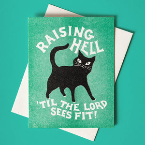 Green background with image of black cat with white text says, "Raising hell until the Lord sees fit!". White envelope is included. 