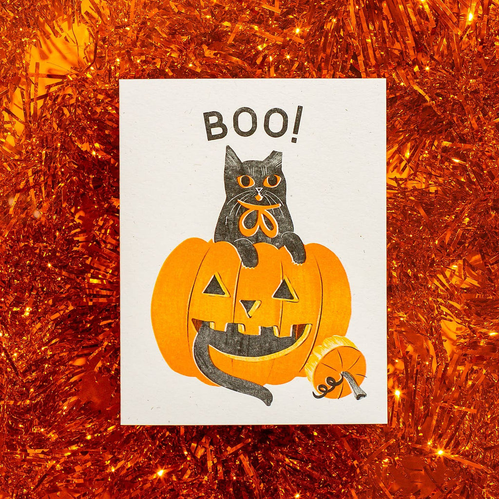 Greeting card with cream background and image of a black cat with a jack o'lantern and black text says, "Boo!". Envelope included.