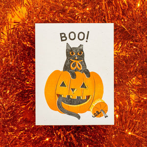 Greeting card with cream background and image of a black cat with a jack o'lantern and black text says, "Boo!". Envelope included.