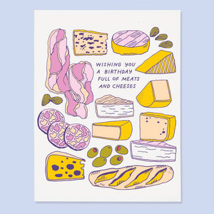 Greeting card with white background with images of meats and cheeses in yellow, lilac, pink and green with purple text says, "Wishing you a birthday full of meats and cheeses". Envelope included.