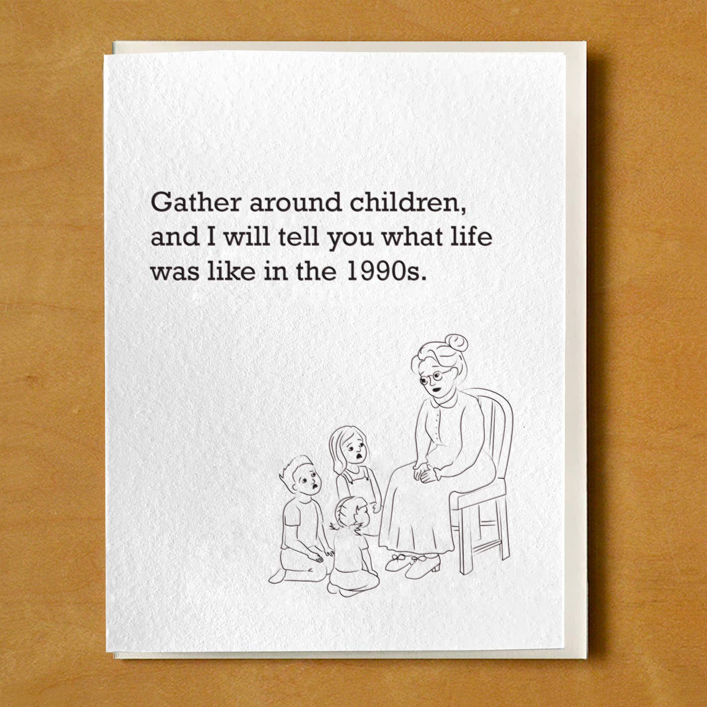 Greeting card with white background and an image of an old woman sitting in a chair addressing three children. Black text says, "Gather around children, and I will tell you what life was like in the 1990s." Envelope included. 