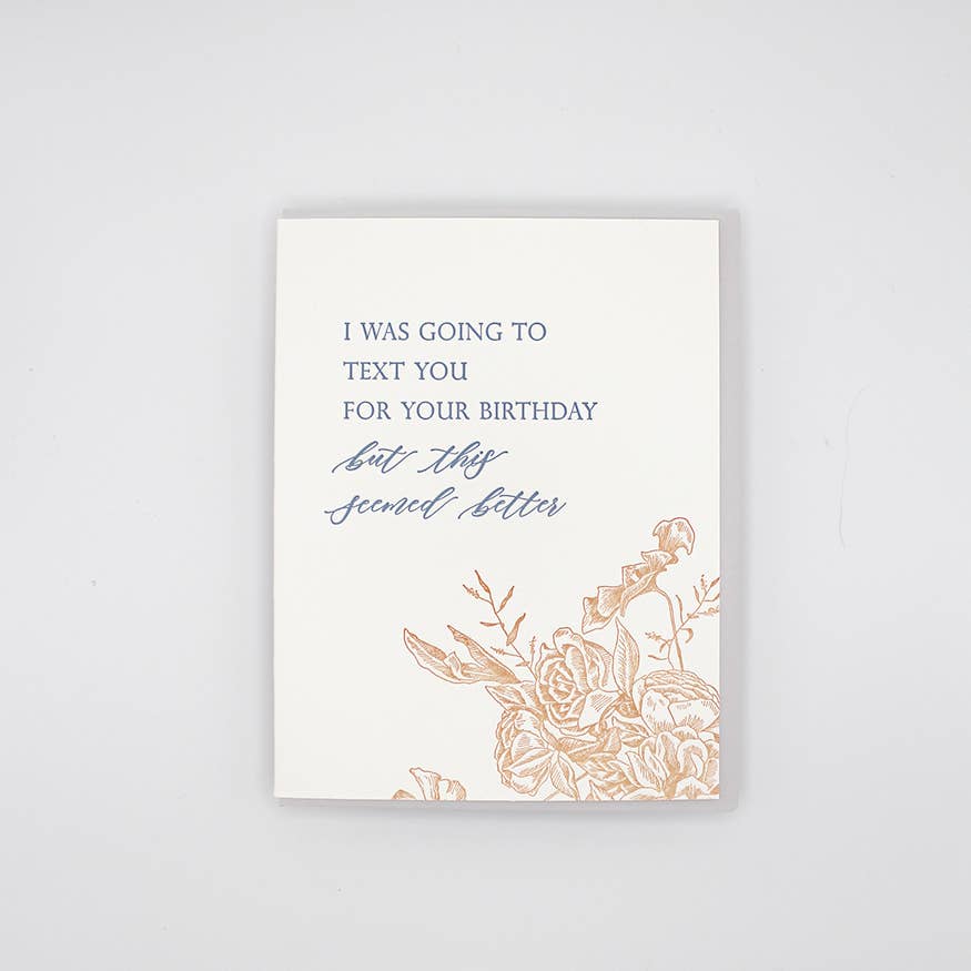 Greeting card with white background and image of flowers in sepia and grey text says, "I was going to text you for your birthday but this seemed better". Grey envelope included.