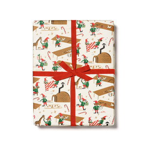 Gift wrap with cream background and images of elves working in Santa's workshop in red, green, brown and white. 