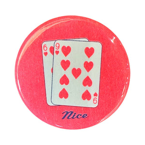 Image of metal button with orange/red background with image of two playing cards with red hearts and 6 and 9. Blue text says, "nice". 