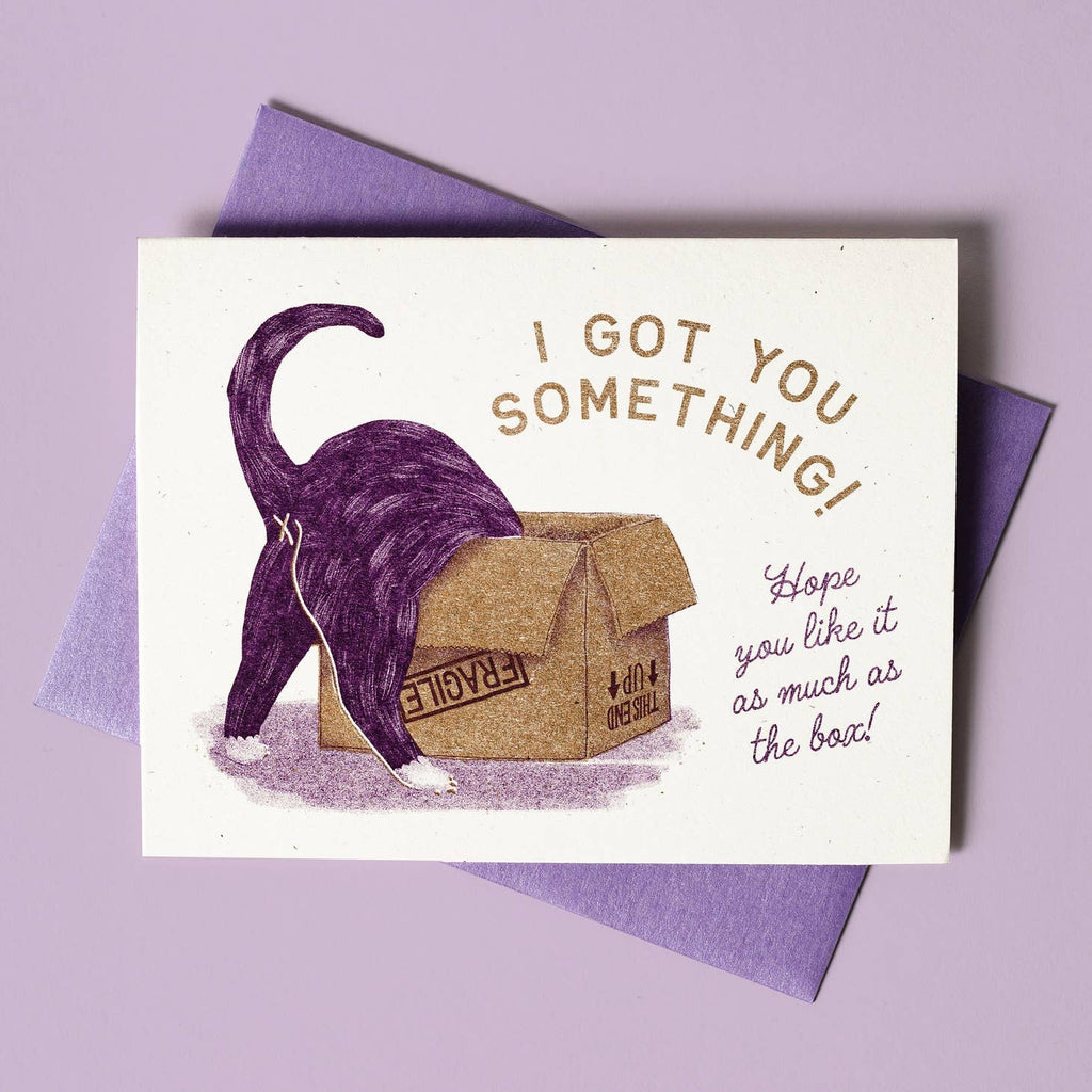 Ivory background with image of a purple cat from behind diving into a cardboard box marked fragile. Gold text says, "I got you something!" and purple text says, "Hope you like it as much the box!". Purple envelope is included. 