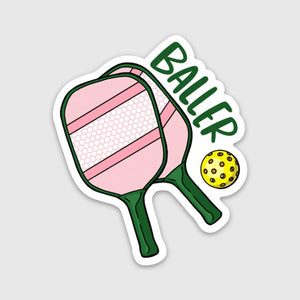 Decorative sticker with image of paddles in pink, white and green and yellow ball. Green text says, "Baller". 