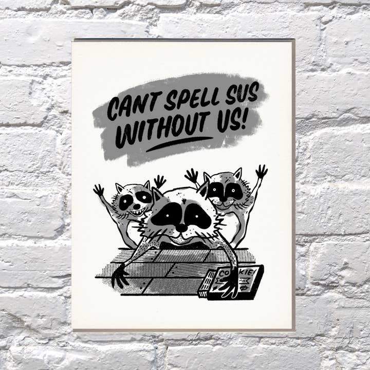 Greeting card with ivory background and images of three raccoons in black and grey with black text says, "Can't spell Sus without us!" Grey envelope included.