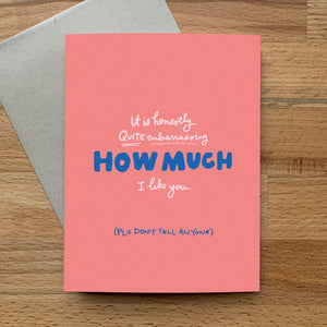 Greeting card with pink background and white and blue text says "It is honestly quite embarrassing how much I like you. Please don't tell anyone". Grey envelope included, 