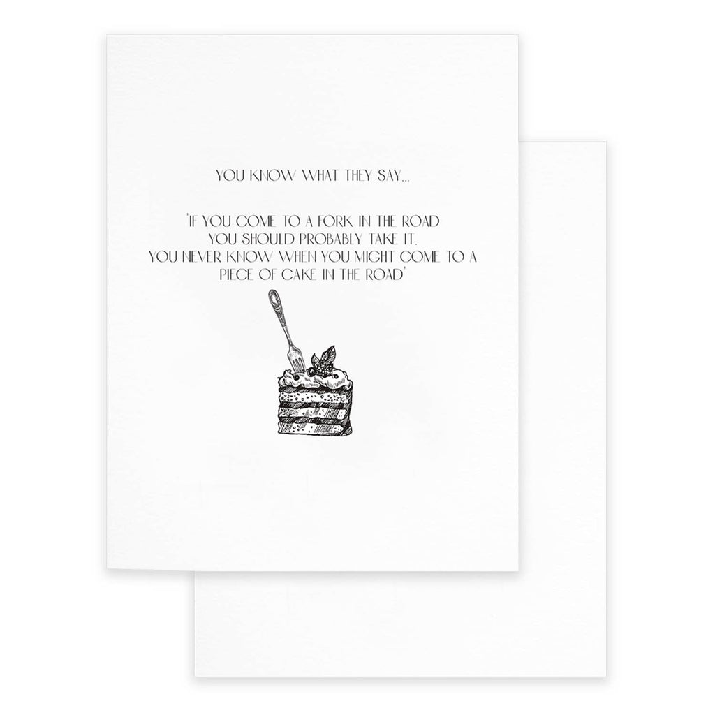 Greeting card with white background and black text says, "You know what they say...If you come to a fork in the road you should probably take it. You never know when you might come to a piece of cake in the road". Image of a slice of cake with a fork stuck in it. White envelope included. 