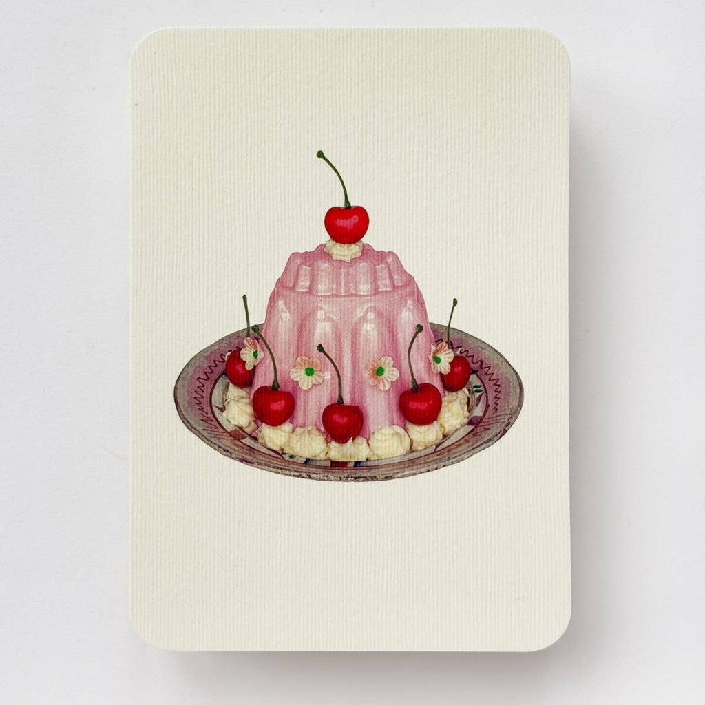 Greeting card with cream background and image of rose blancmange dessert with cherries on pink plate. Envelope included.