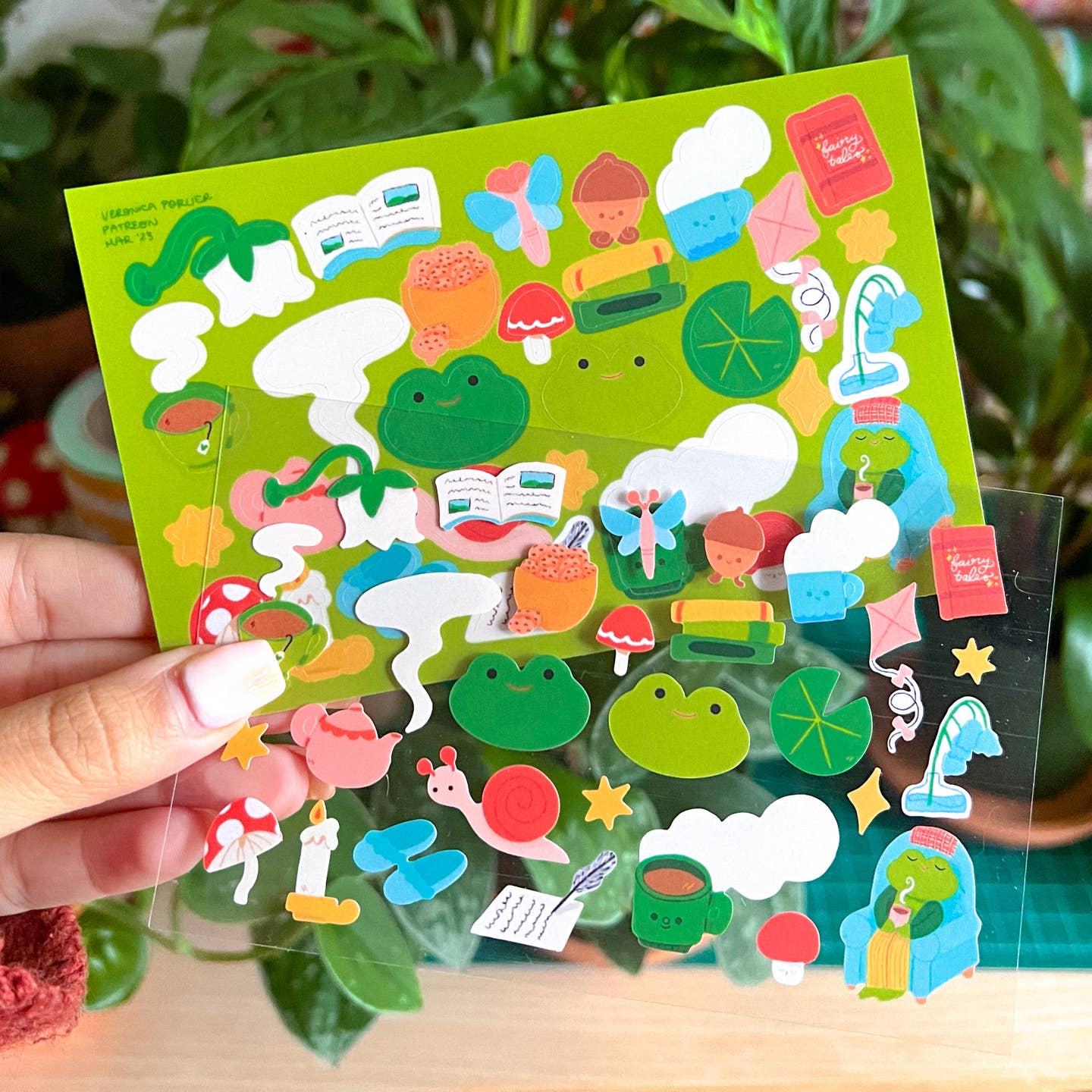 Decorative sticker sheet with green background and iamges of frogs and toads with various items like mushrooms, snails, acorns, and flowers. 