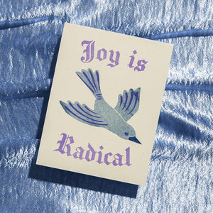 Greeting card with white background and image of a bird flying with lilac text says, "Joy is radical". Envelope included. 