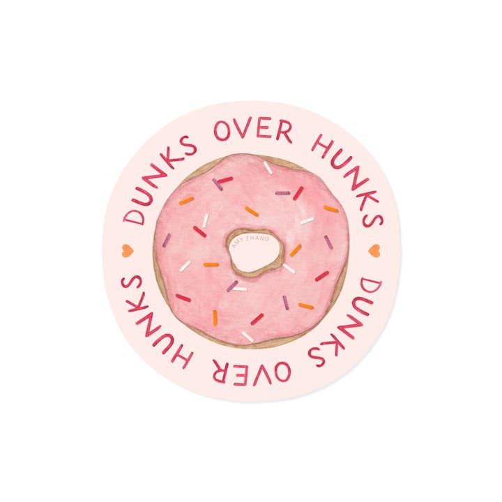 Image of circular sticker with pale pink background  and image of pink frosted donut with sprinkles and red text says, "Dunks over hunks, dunks over hunks". 