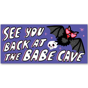 Decorative bumper sticker with purple background with white text says, "See you back at the Babe Cave". Image of a black bat wearing heart shaped pink glasses and holding a skull. 