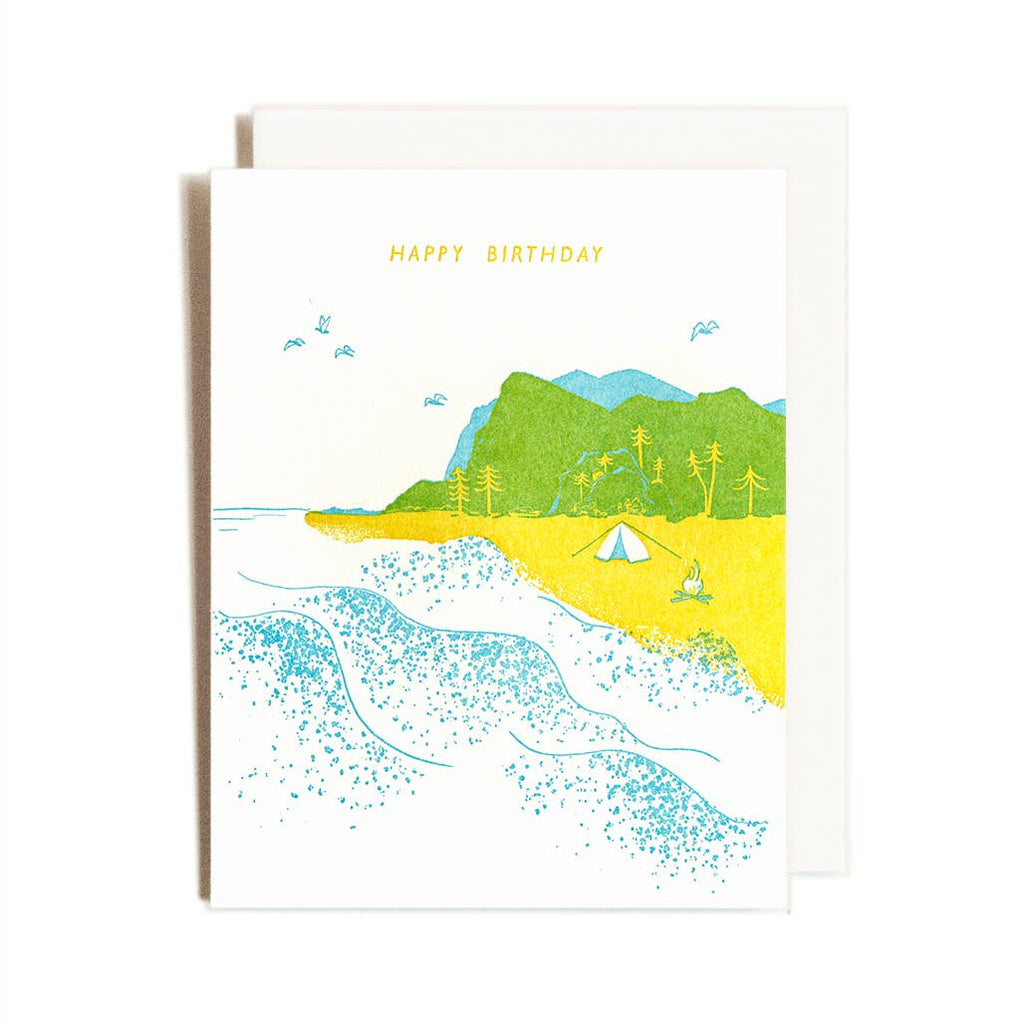 greeting card with a beach scene. Blue ocean, yellow sand and green and blue mountains in the background.
