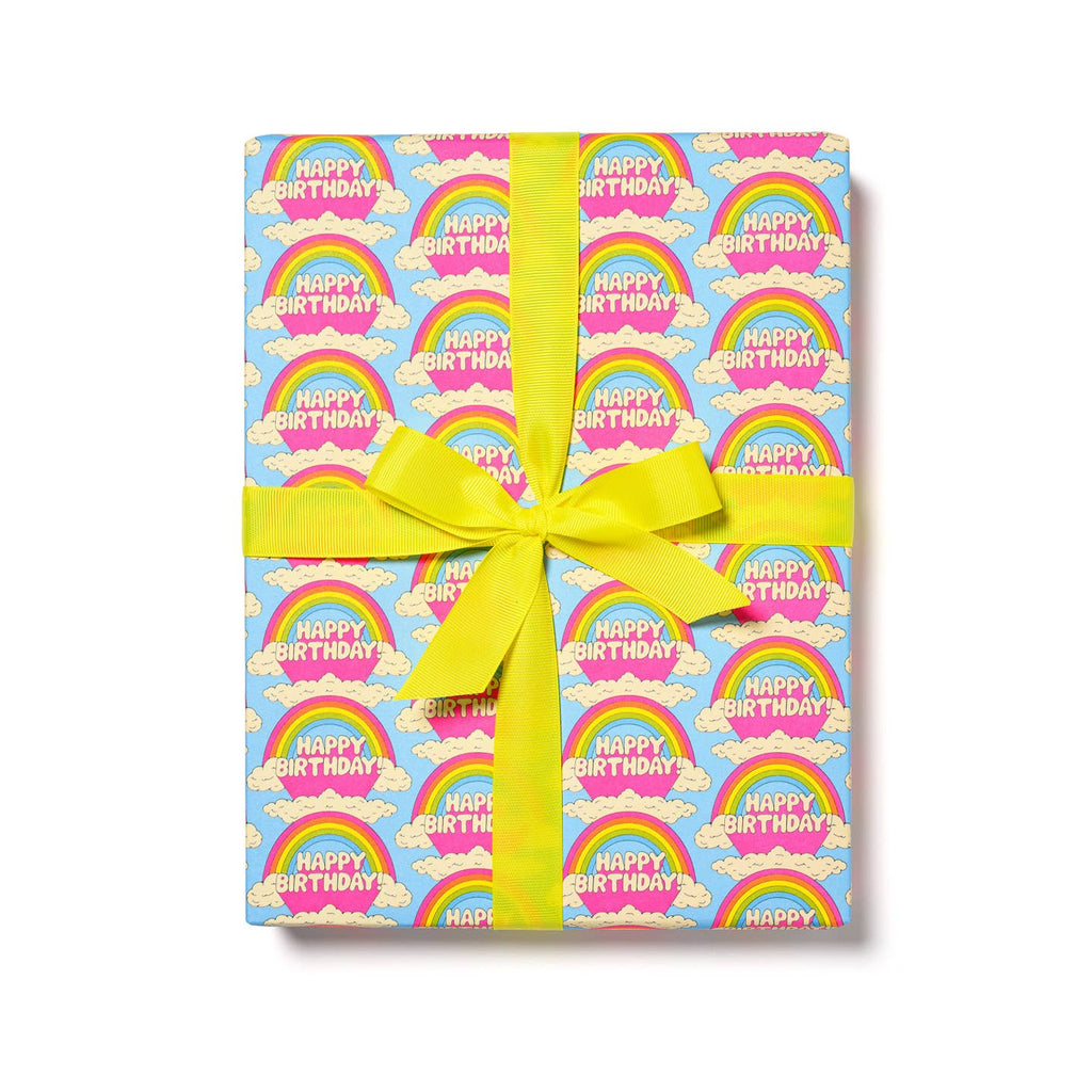 Gift wrap with light blue background and images of rainbows and clouds with white puffy text says, "Happy Birthday". 