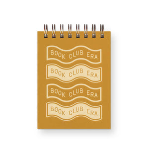 Small notebook with saffron colored cover with white text says, "Book club era" four times on wavy banners. Coil binding on top. 