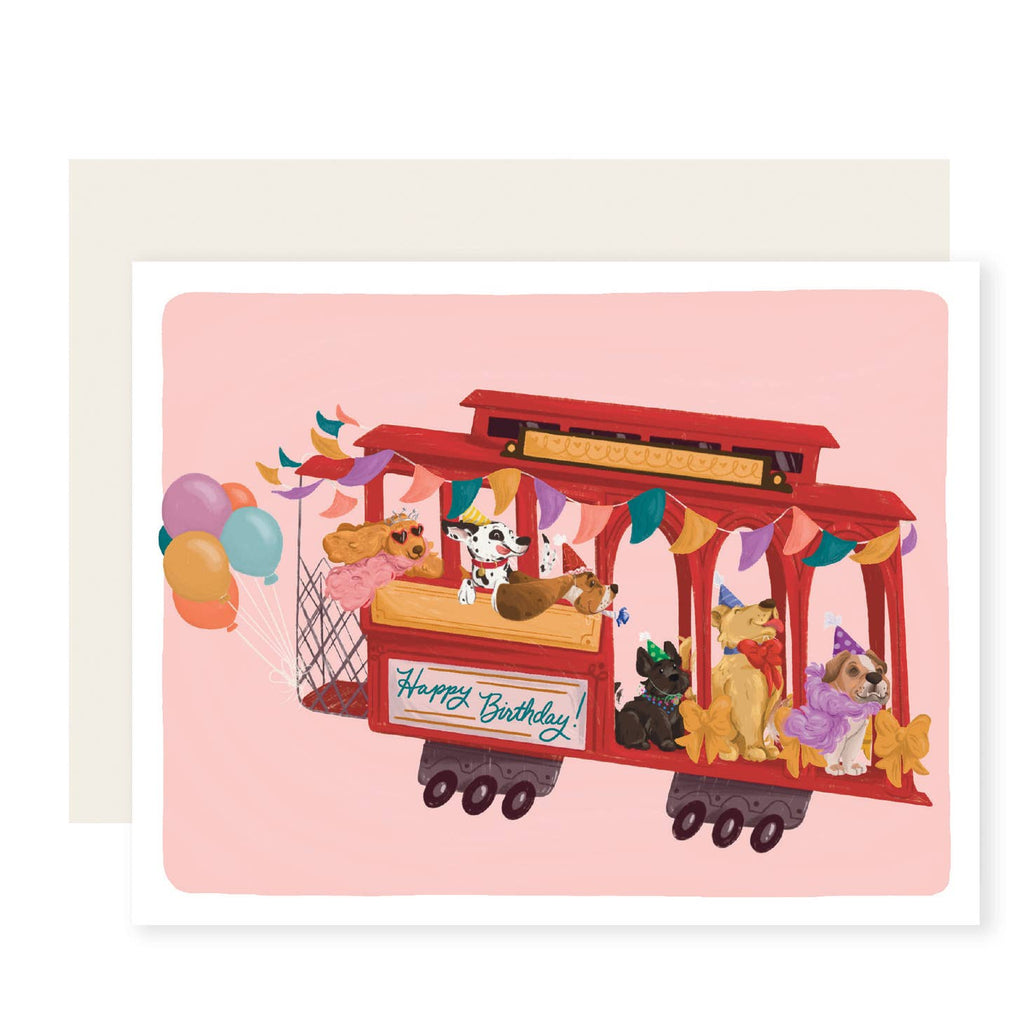Greeting card with pink background and red cable car filled with dogs wearing party hats and blue text says, "happy birthday!". Cream envelope included. 