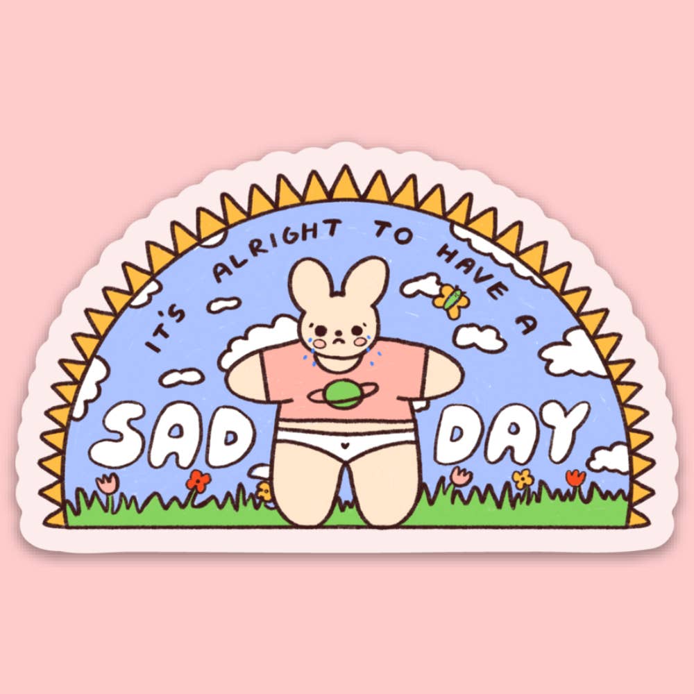 Decorative sticker with blue background and image of a tan bunny standing in a field of flowers and black and white text says, "It's alright to have a sad day". 