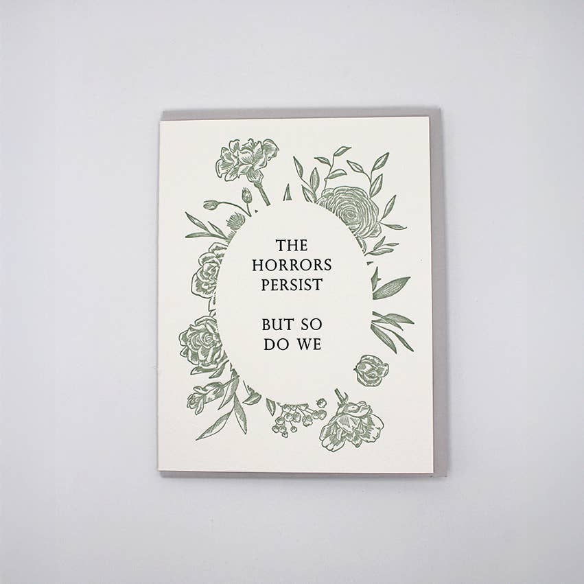 Greeting card with white background and grey oval of flowers and text says, "The horrors persist,but so do we". Grey envelope included.