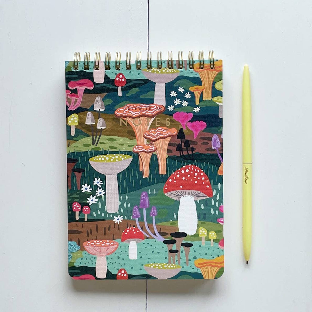 Notepad with cover images of mushrooms in bright colors of red, yellow, white teal and pink. Coiled binding at top. 