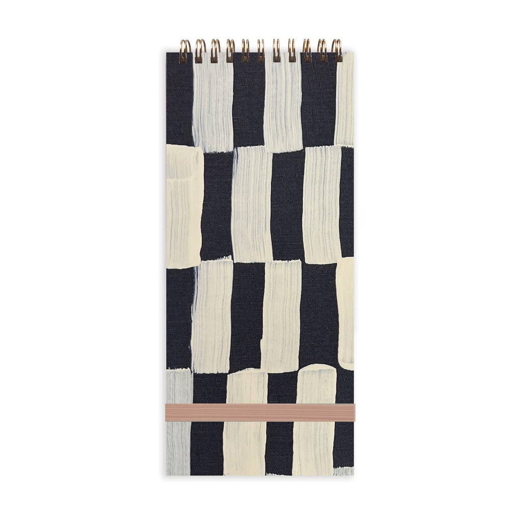Image of notebook front with black and white sweeps of paint in checkerboard pattern with tan elastic enclosure and wire binding at top. 