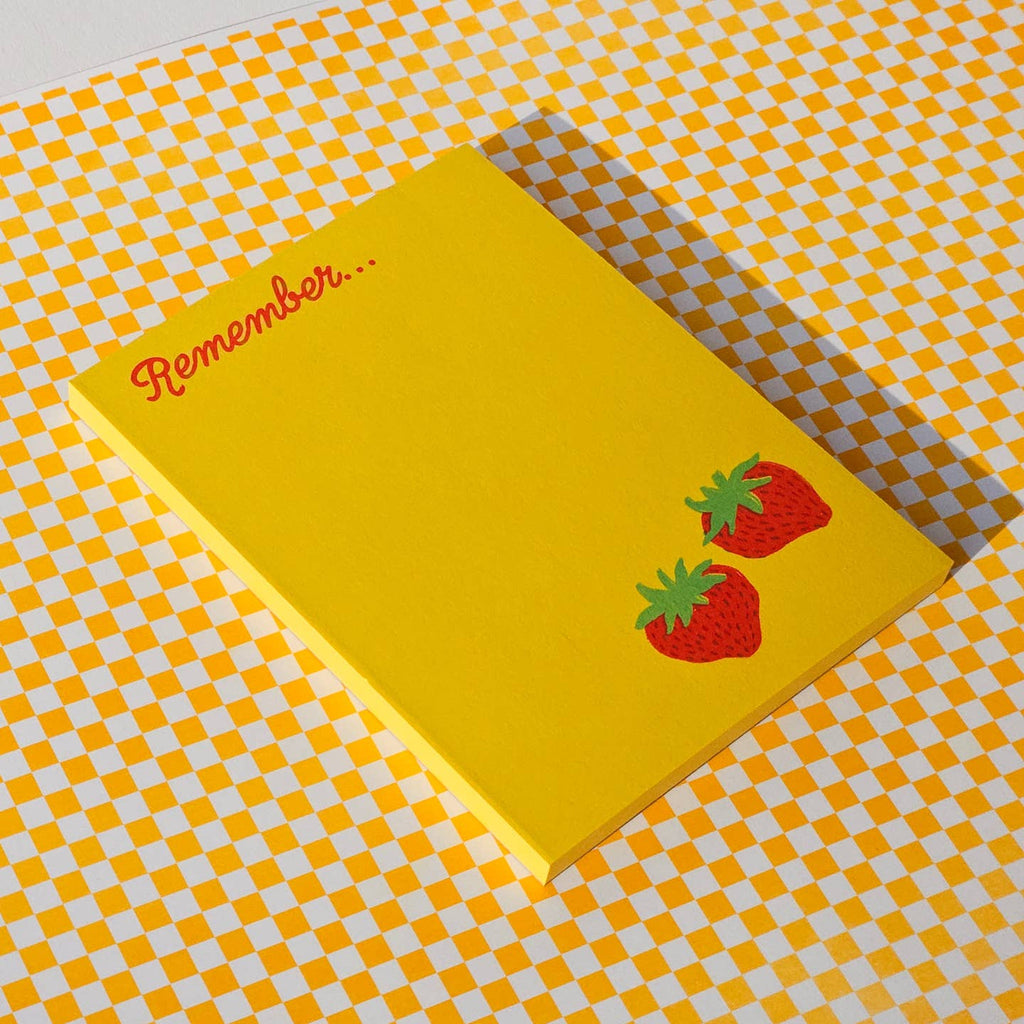Notepad with yellow background with image of two red strawberries with green stems in bottom right corner and red text says, "Remember..." at top of pad. 