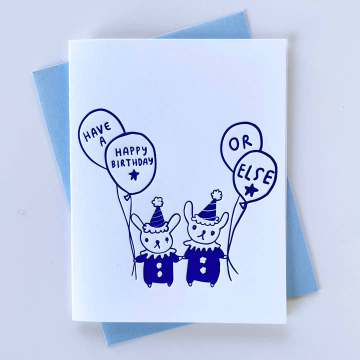 Greeting card with white background with image of tow clown bunnies holding balloons. Purple text says, "Have a happy birthday or else". Blue envelope included. 