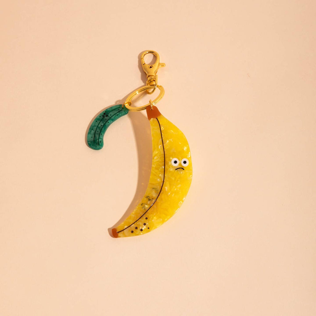 Image of a plastic charm in the shape of a green pickle and a yellow banana with a face.