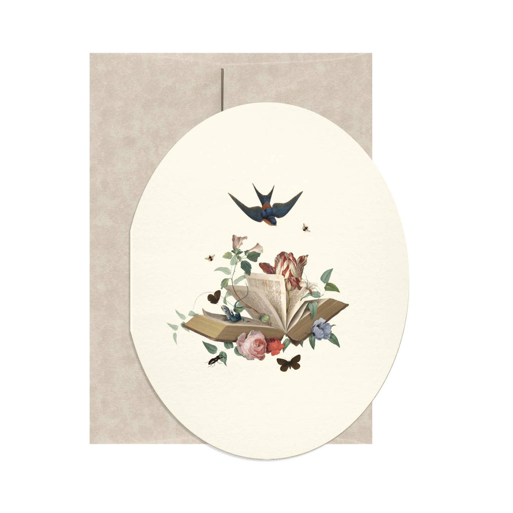 Oval shaped greeting card with cream background and image of an open book with flowers blooming out of it and a blue bird flying above it. Tan envelope included.