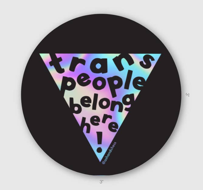 Circular sticker with black background with inverted holographic triangle with black text says, “Trans people belong here!”.    