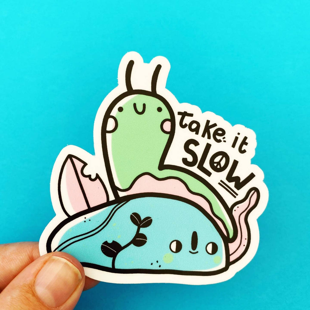 Image of sticker with image of green and pink snail and a blue rock and pink leaf. Black text says,"take it slow" with peace sign in the "o" of slow. 
