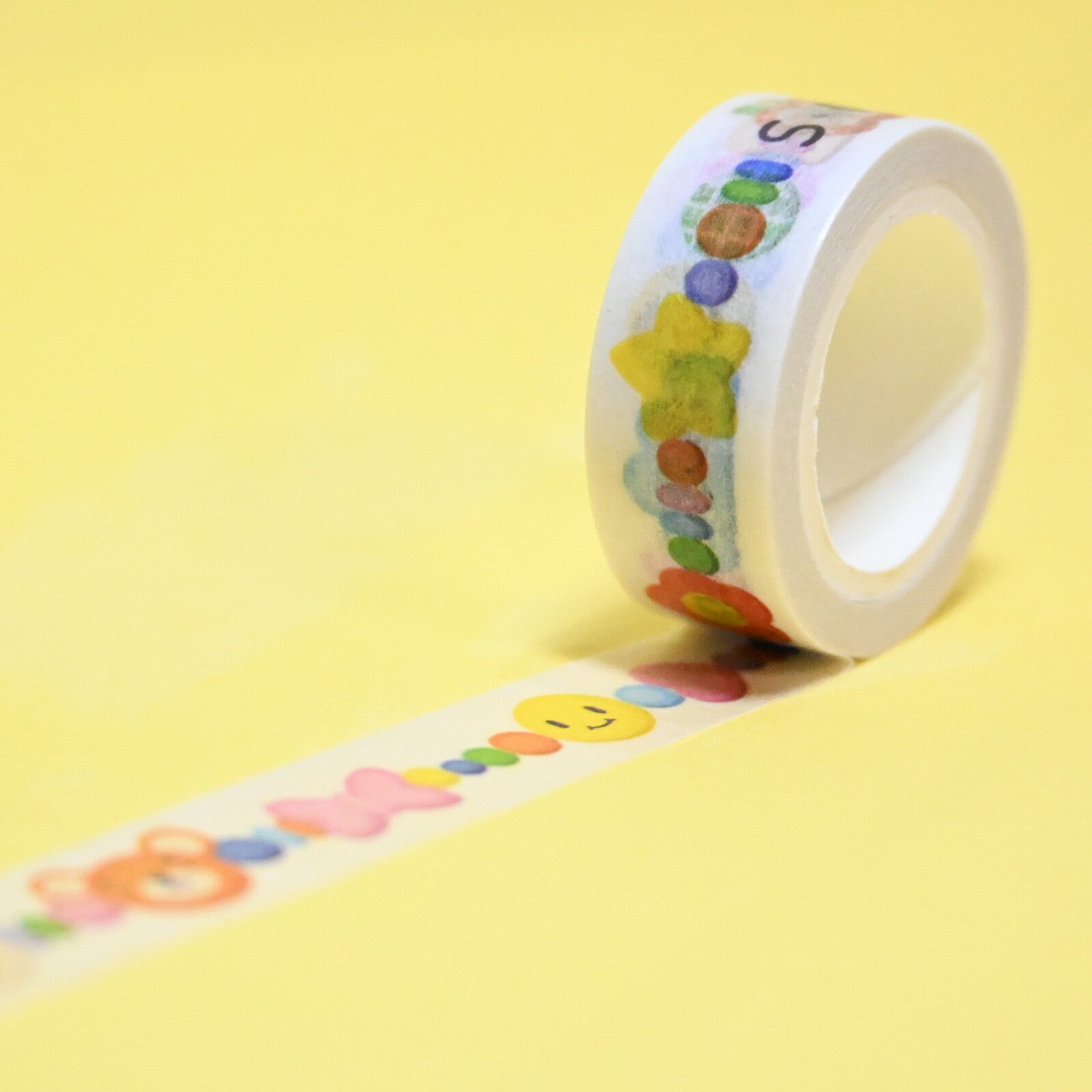 Roll of decorative tpe with clear background and images of beads and letters in different colors.