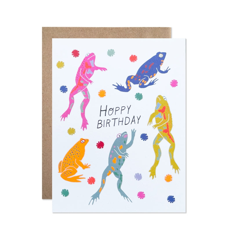 White card with black text saying, “Hoppy Birthday”. Images of colored frogs and lily pads. A brown envelope is included.