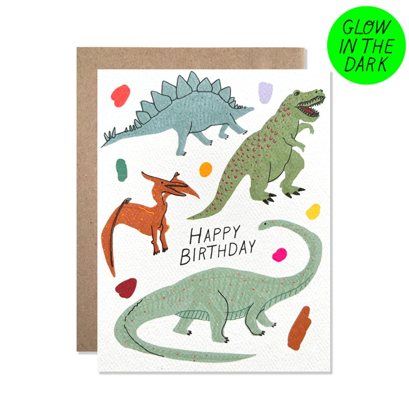 White card with black text saying, “Happy Birthday”. Images of various dinosaurs with colored dots in background. Card glows in the dark. A brown envelope is included.
