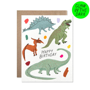 White card with black text saying, “Happy Birthday”. Images of various dinosaurs with colored dots in background. Card glows in the dark. A brown envelope is included.