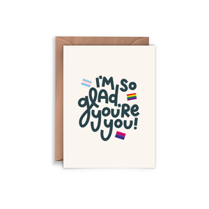 Ivory card with black text saying, “I’m So Glad You’re You!”  Images of several sexual identity group flags on card. A brown envelope is included.