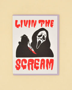 White card with red scary text saying, "Livin the Scream". Image of a person wearing a mask holding a bloody knife. A purple envelope is included.